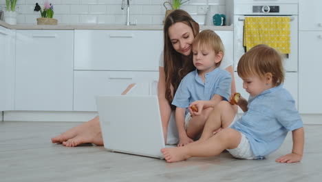 Modern-technology.-Modern-apartment-loving-mom-and-two-small-sons-sitting-on-the-floor-in-the-living-room-look-at-the-laptop-screen.-Children-with-mom-play-on-a-laptop.